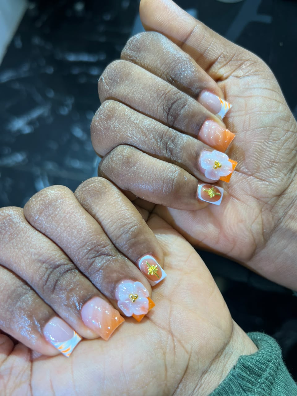 Square nails with 3D white flowers, orange French tips, and gold star accents