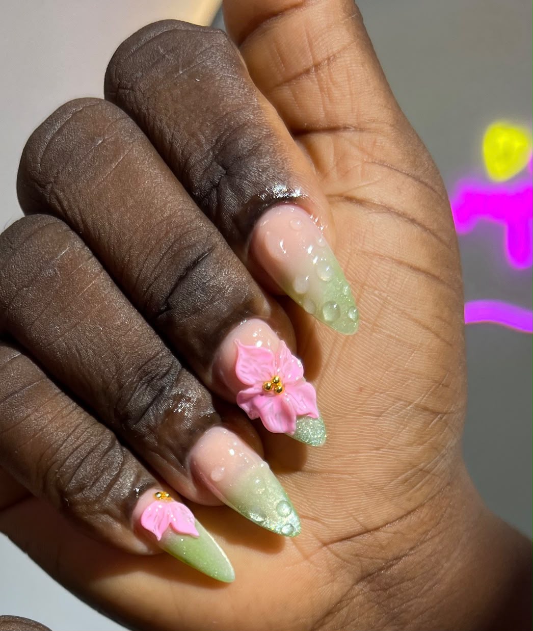 Stiletto nails with 3D pink flowers, green glitter ombre, and dewdrop effect