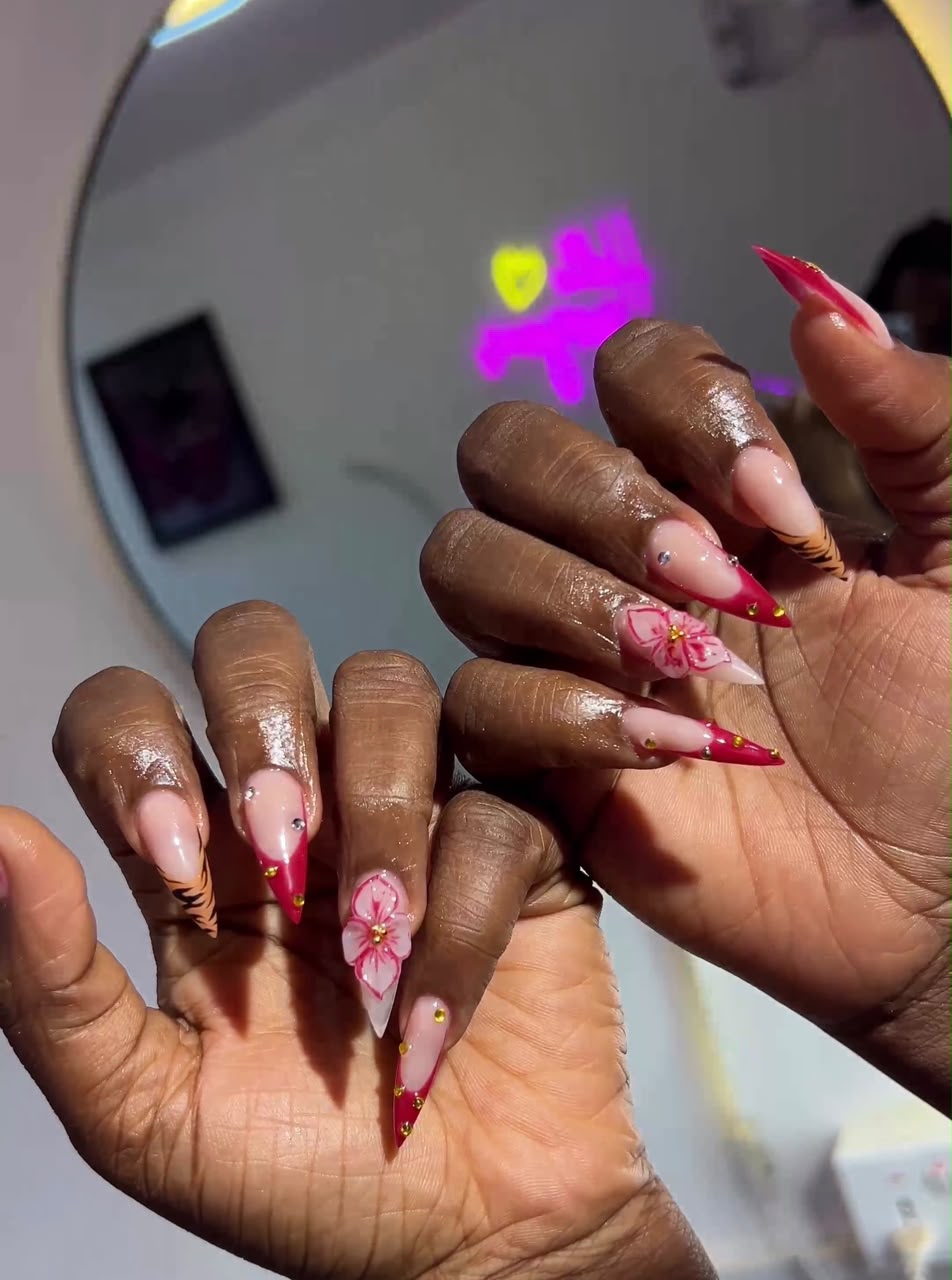 Stiletto nails with pink tiger print, red tips, 3D pink flowers, rhinestones and gold accents